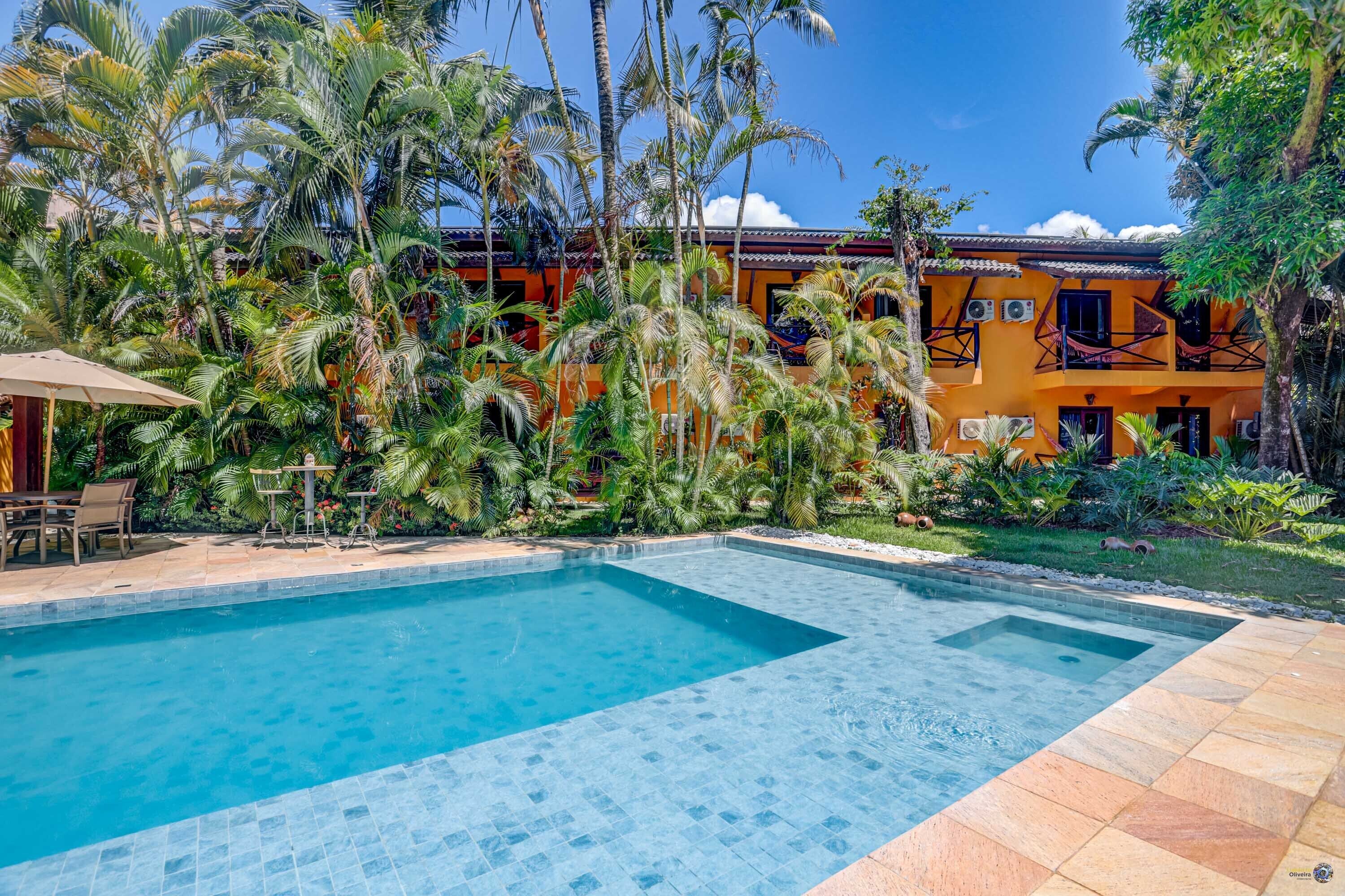 A swimming pool with a tiled deck, surrounded by lush greenery and palm trees.