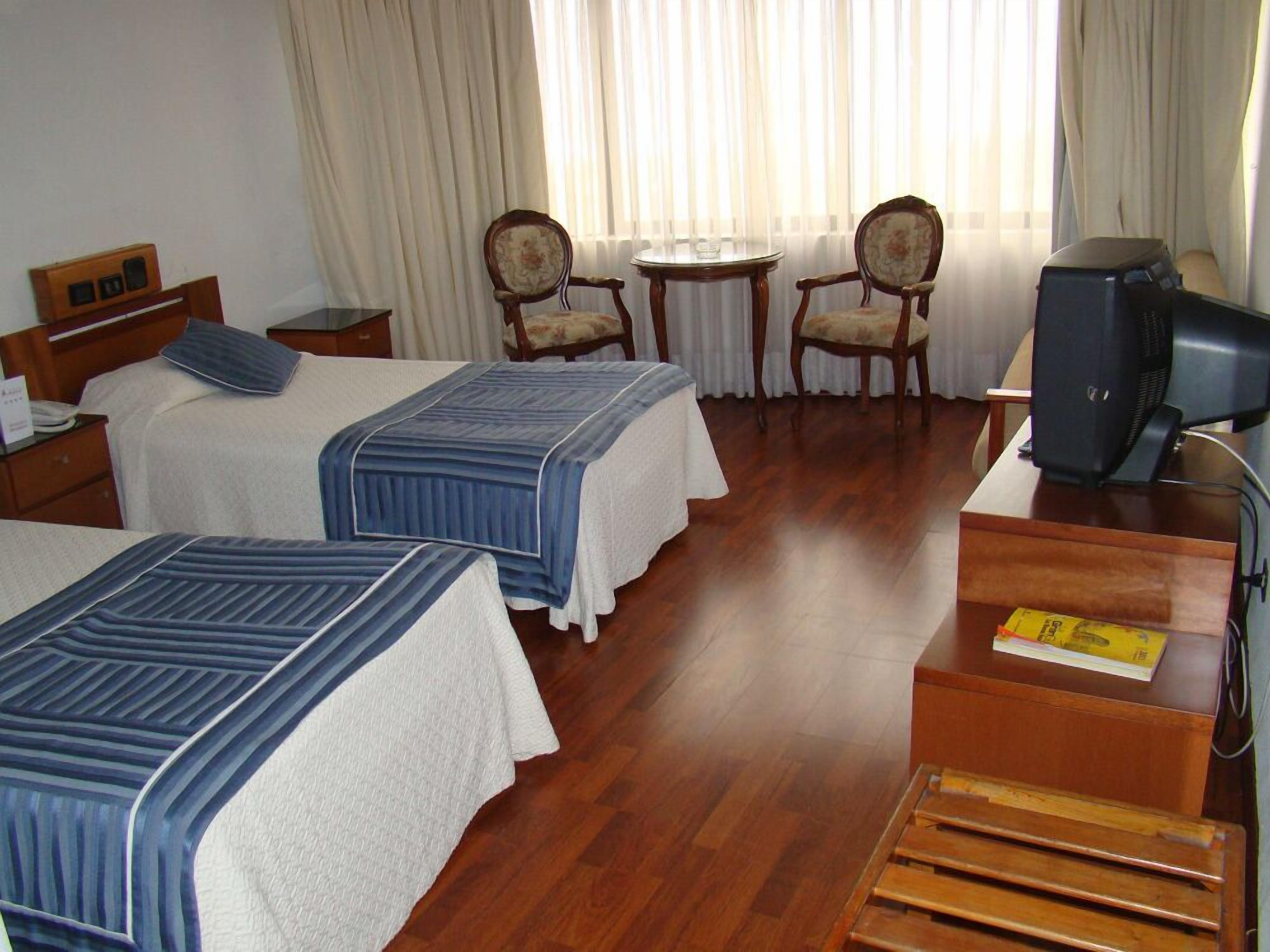 A hotel room with two beds, a desk, a television, and two chairs.