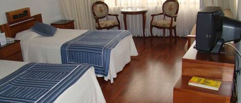 A hotel room with two beds, a desk, a television, and two chairs.