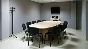A conference room with a large oval table, black chairs, a standee, a flat-screen TV, and a speaker system. - Sunset Kosharitsa (KOSHARITSA)