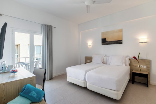 Habitación de hotel con dos camas, un escritorio con silla, una mesita pequeña y una obra de arte colgada en la pared.