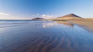 Une plage avec une rive sablonneuse et une colline en arrière-plan.