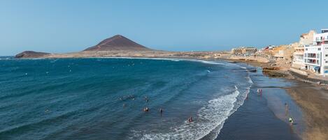 Una playa costera con aguas azules cristalinas, una orilla arenosa y una montaña al fondo.