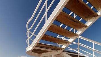A deck with a metal railing and wooden slats, overlooking a body of water with a distant landmass.