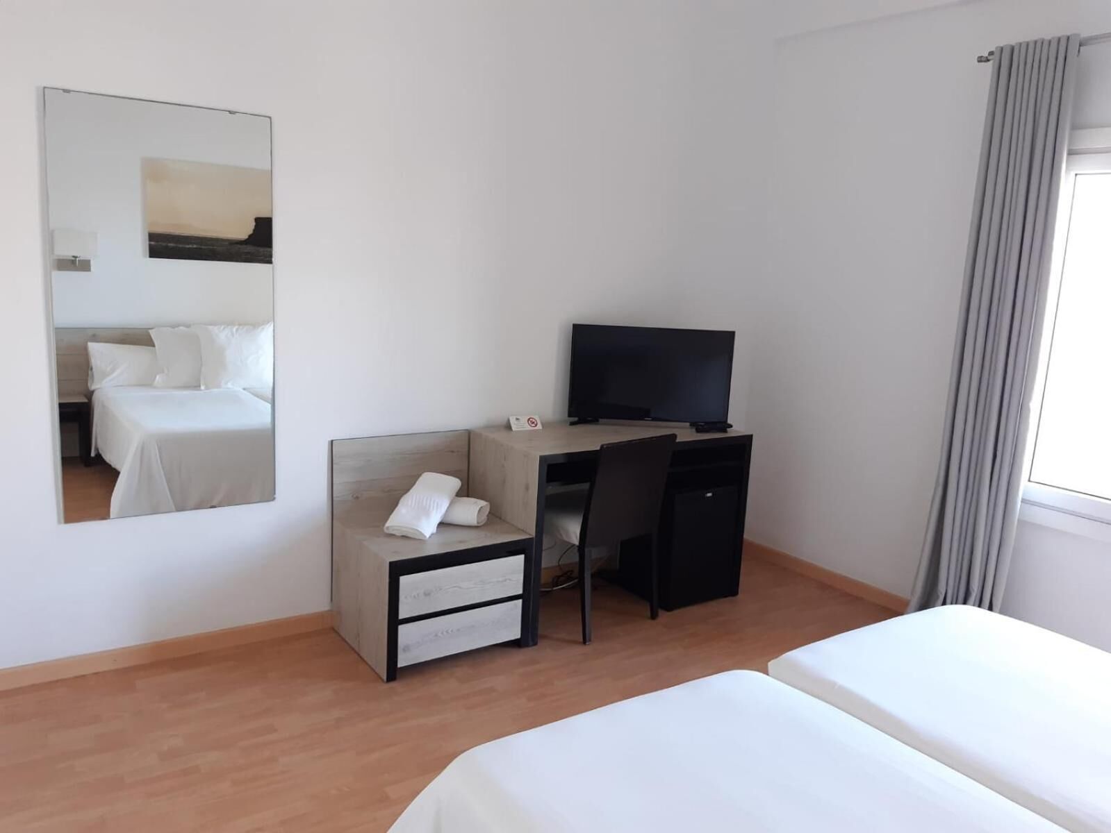 A hotel room with a bed, a desk with a computer, a chair, a TV, and a mirror.