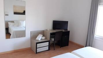 Habitación de hotel con cama, escritorio con computadora, silla, televisor y espejo.