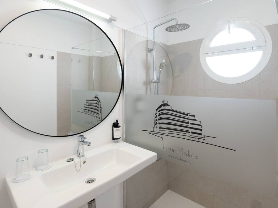 A modern bathroom with a round mirror, a white sink, and a glass shower enclosure.