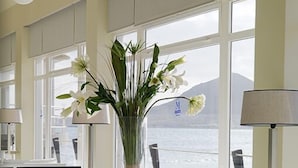 Une pièce moderne dotée d’une grande fenêtre donnant sur un plan d’eau, d’un canapé blanc, d’une table ronde et d’un vase rempli de fleurs.