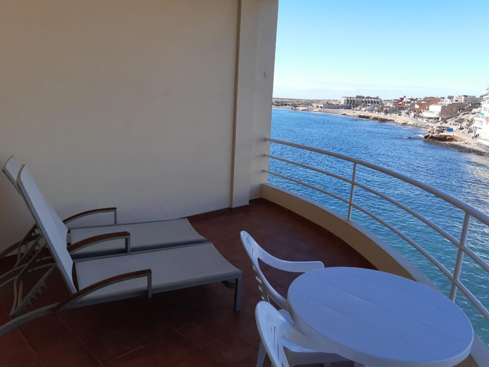 Un balcón con vistas a un pueblo costero, una mesa blanca y dos sillas blancas.