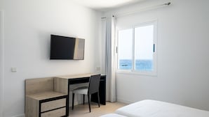 Une chambre à coucher avec un lit, un bureau et une chaise, une télévision et une fenêtre donnant sur la mer.