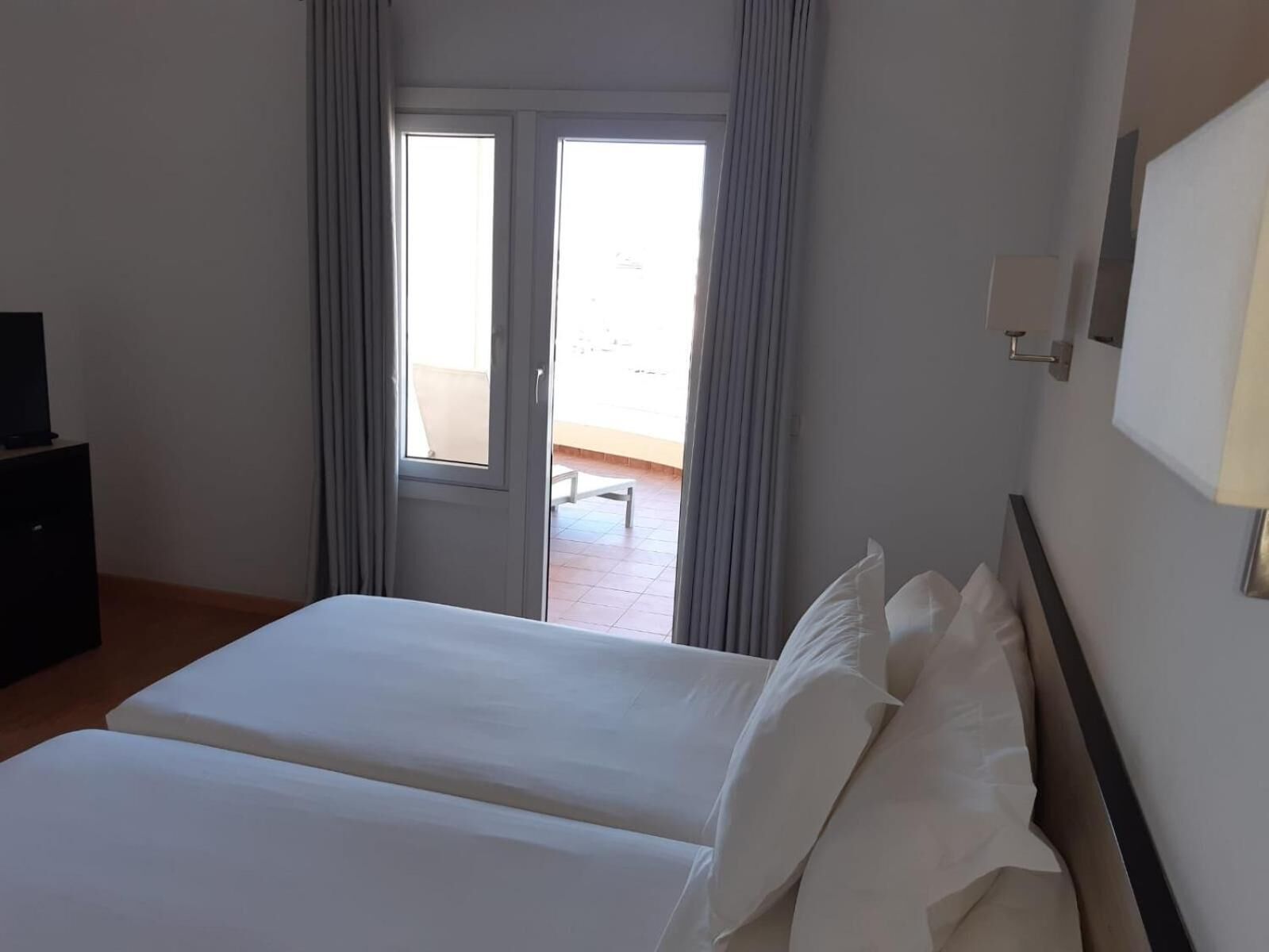 A hotel room with a bed, a television, and a balcony with curtains.