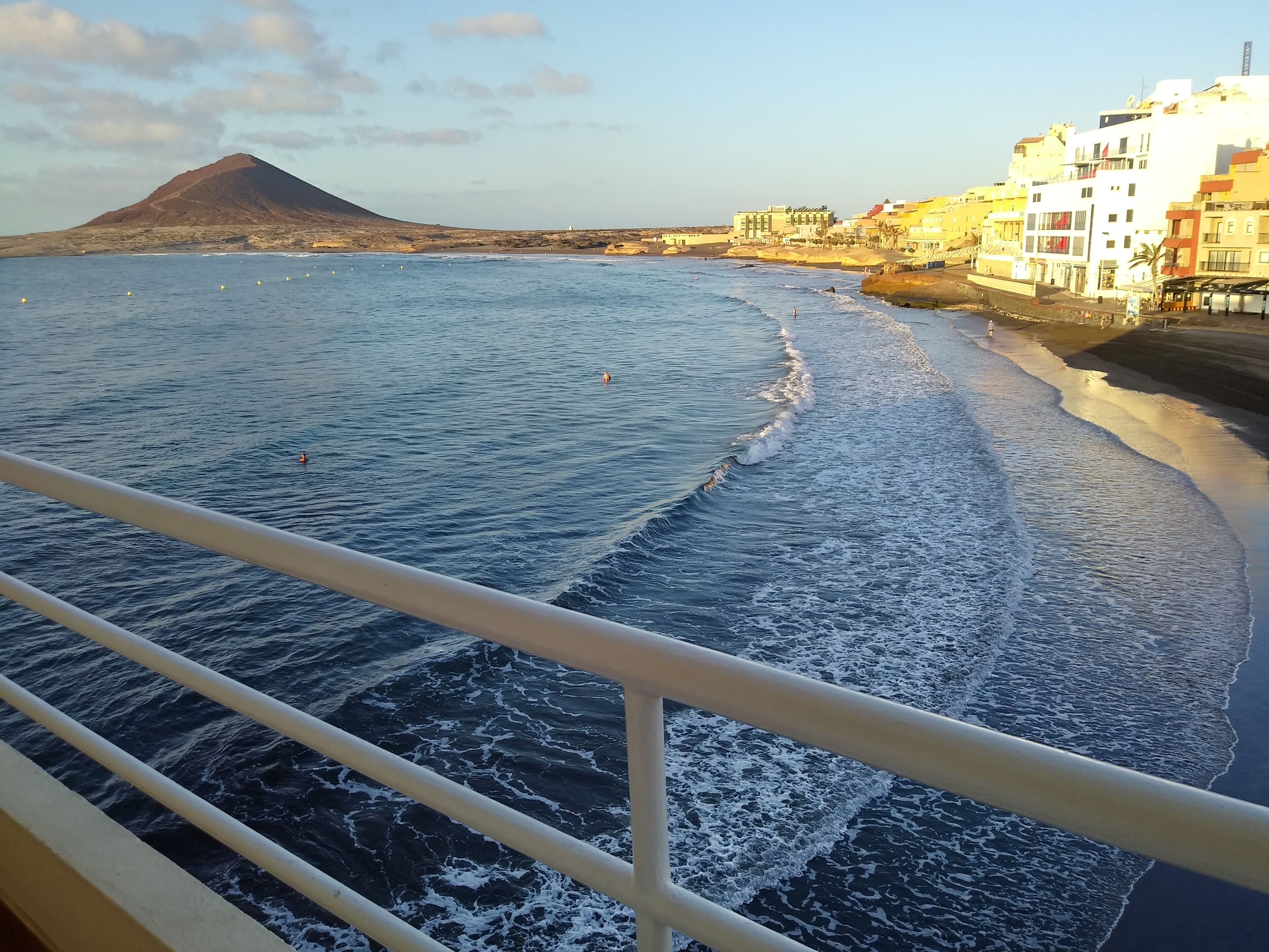 A coastal view with a mountain in the background, a beach, and buildings along the shore.