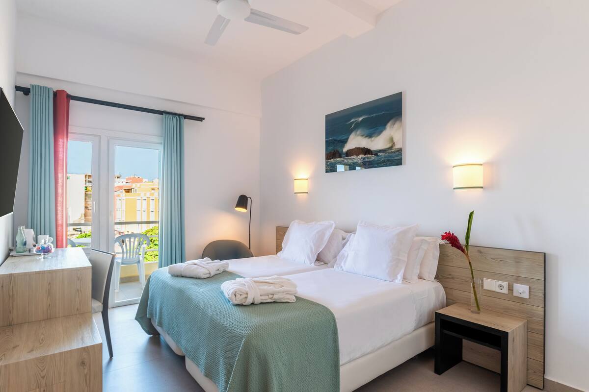 Ein Hotelzimmer mit einem Bett, einem Schreibtisch, einem Sessel, einem Nachttisch, einer Lampe und einem Bild an der Wand.