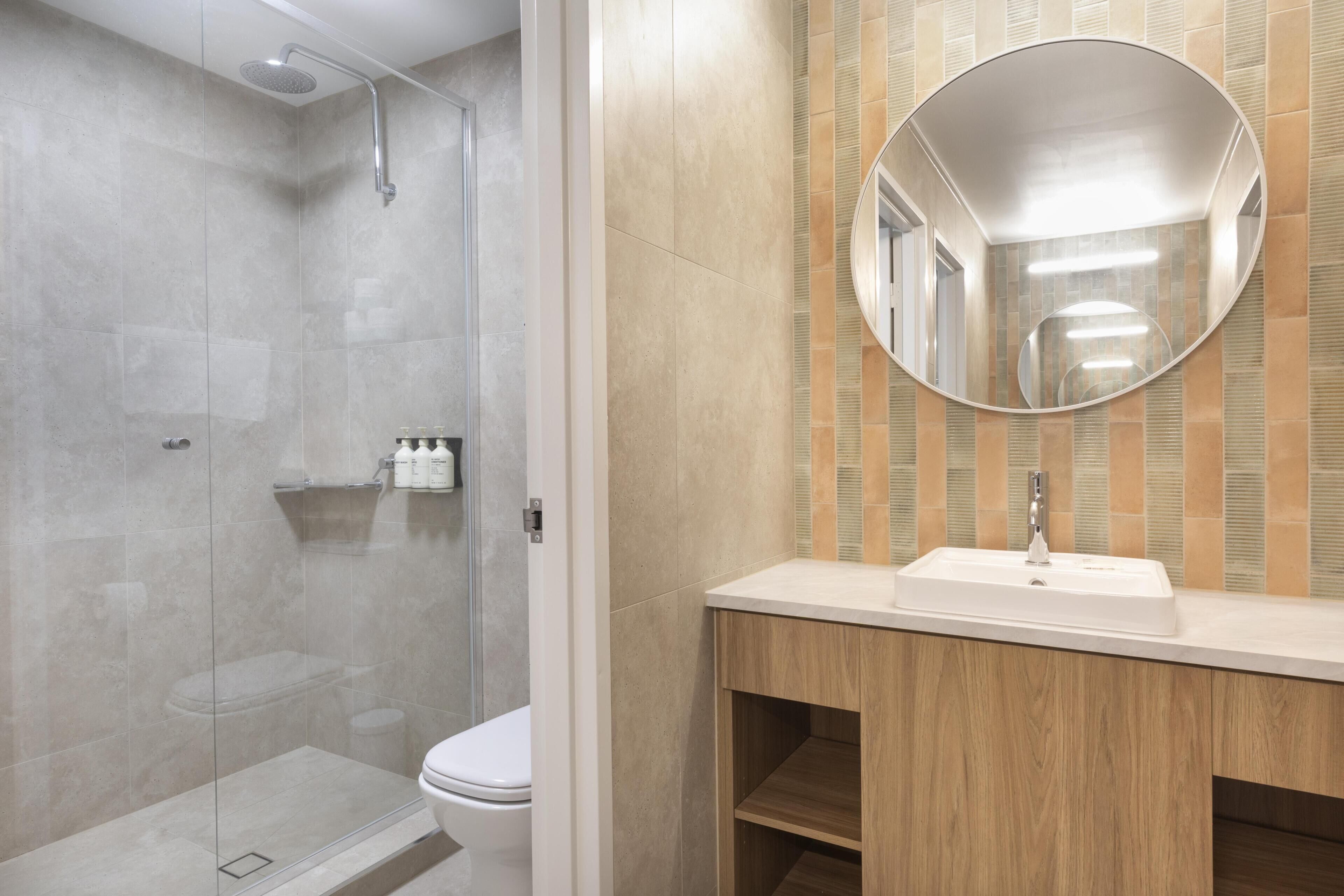 A modern bathroom with a glass-enclosed shower, a toilet, and a vanity with a mirror.