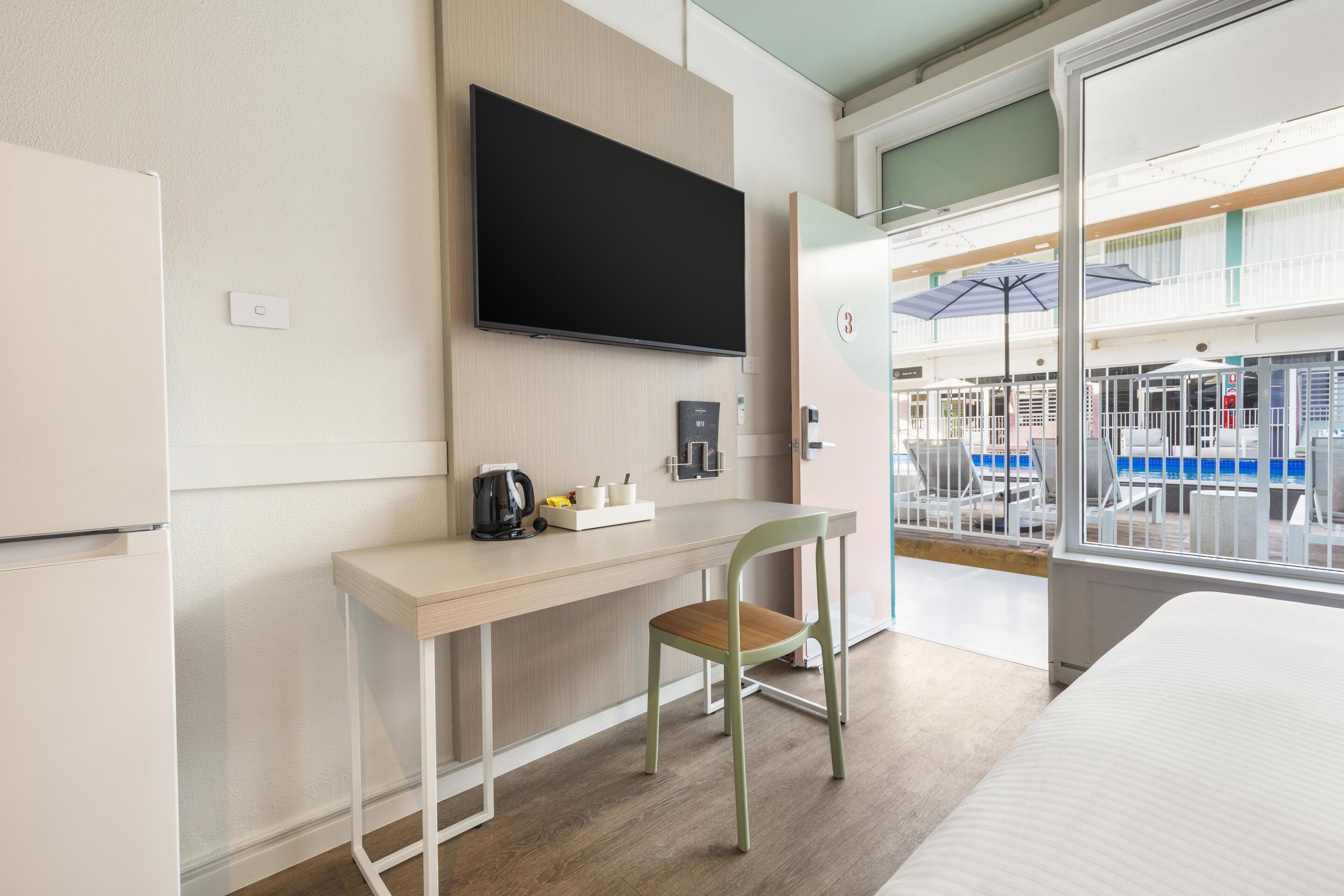 A hotel room with a bed, a desk with a chair, a television, a coffee maker, and a window with a view of the outside.