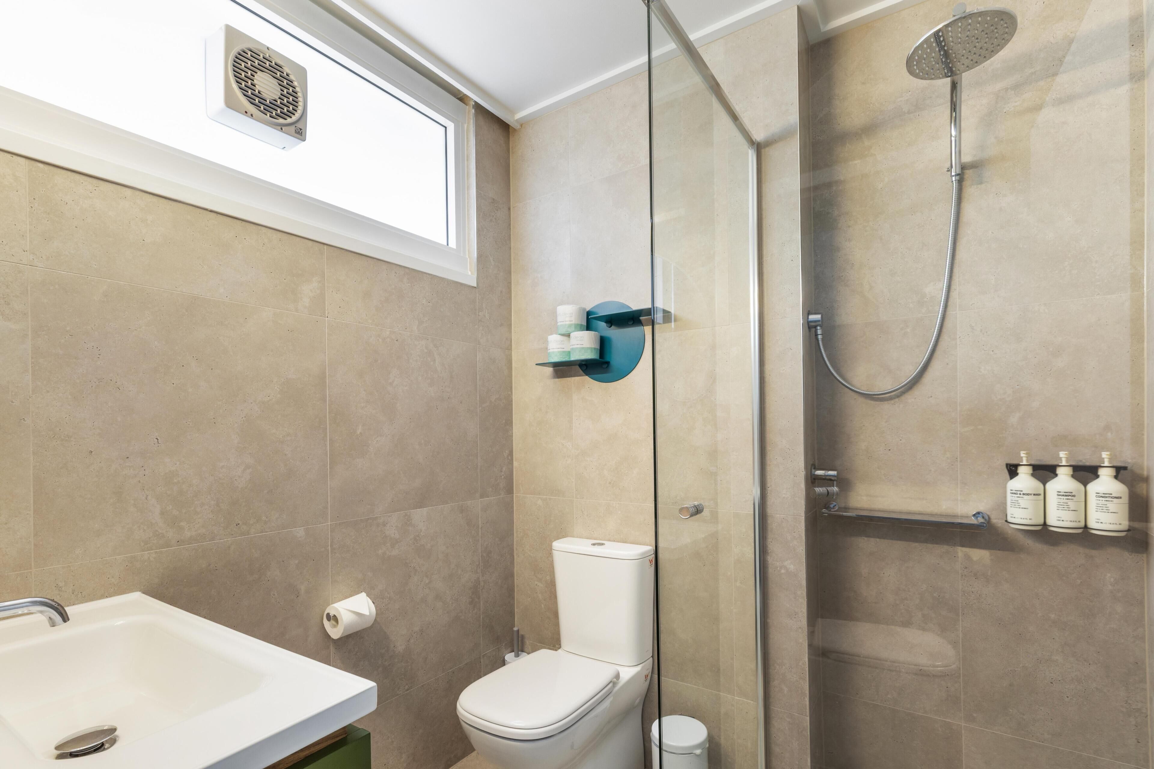 A bathroom with a toilet, a glass-enclosed shower, a sink, and a window above the toilet.