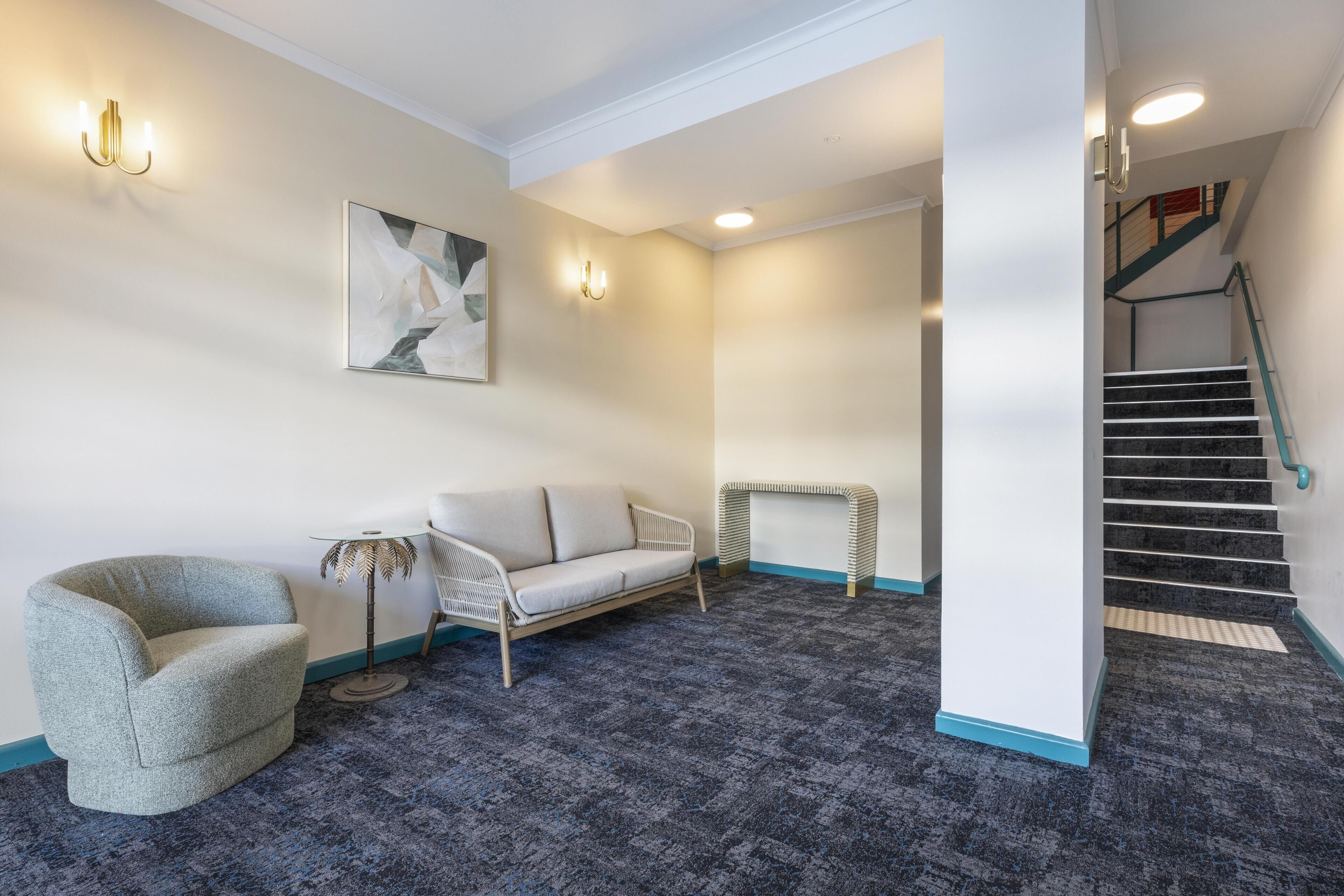 A modern interior with a grey armchair, a white sofa, a small round table, and a staircase with a blue handrail.