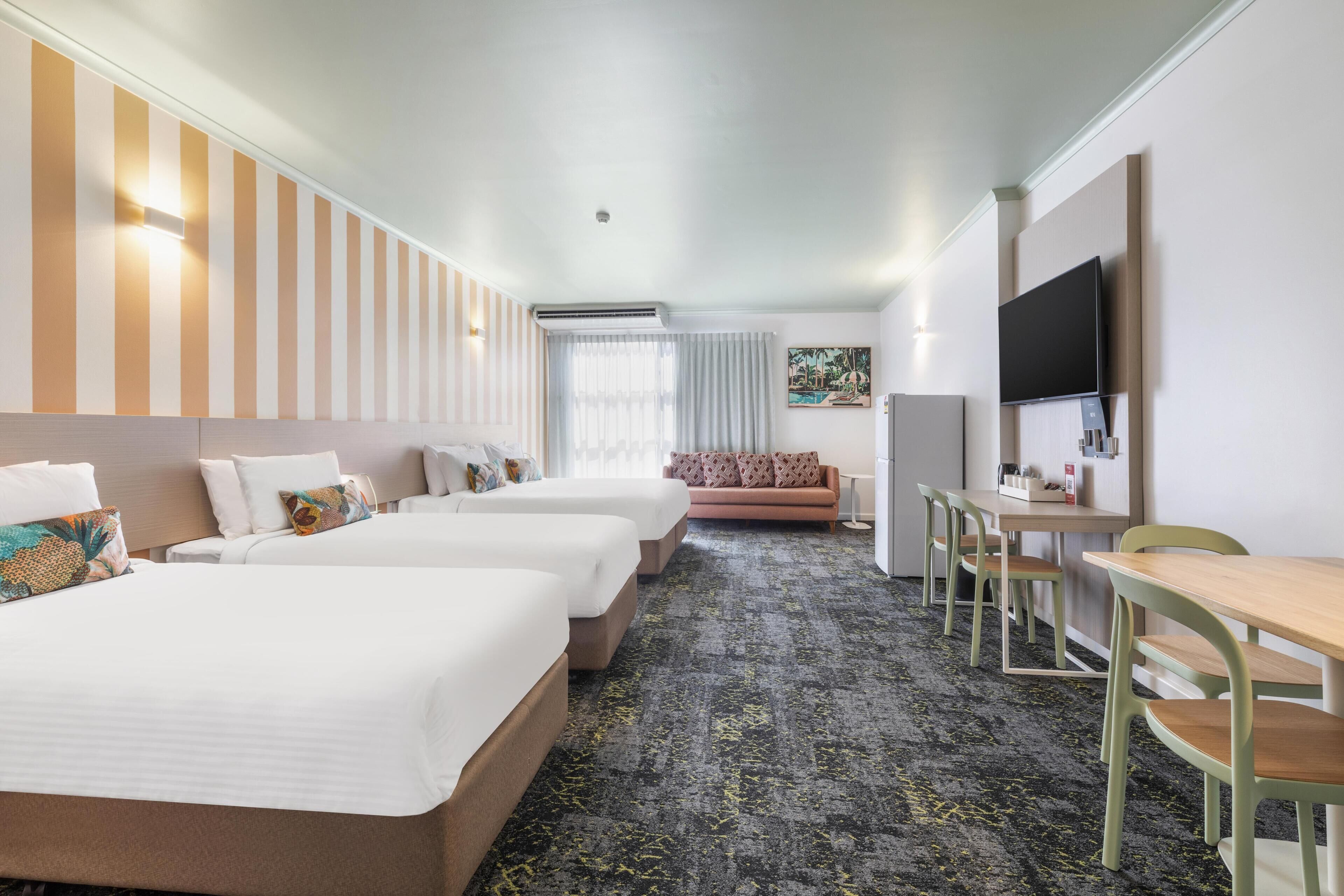 A hotel room with three beds, a sofa, a desk, and a TV.