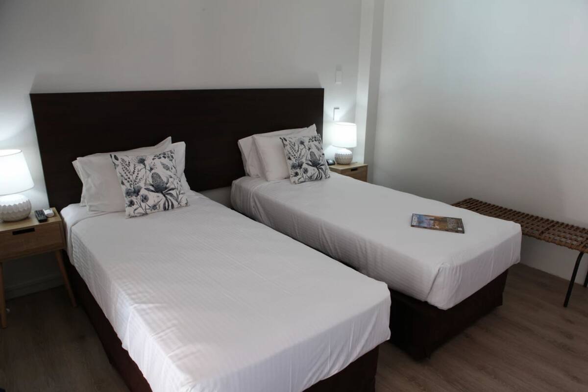 Une chambre d’hôtel avec deux lits, chacun étant équipé d’un oreiller et d’une table de chevet avec une lampe.