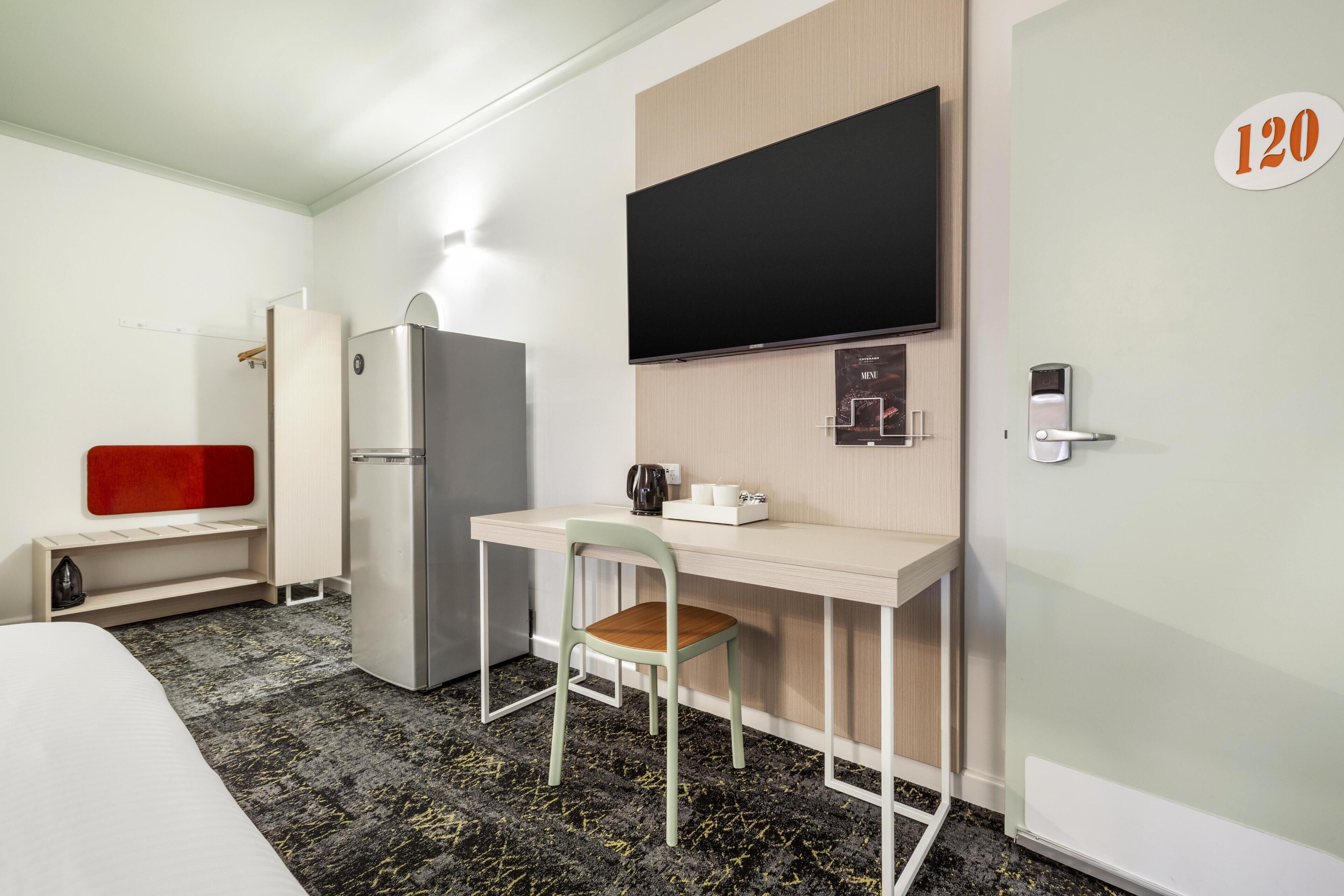 A hotel room with a bed, a desk, a chair, a television, a refrigerator, and a door with the number 120.