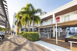An outdoor seating area with tables and chairs, a covered section with a fire hose reel, and a palm tree.