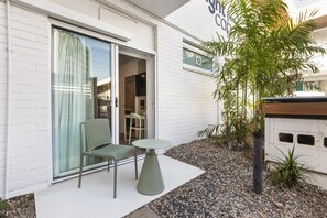 Un edificio moderno con entrada por puerta de vidrio, un pequeño espacio al aire libre con mesa y sillas, y un jardín con diversas plantas.