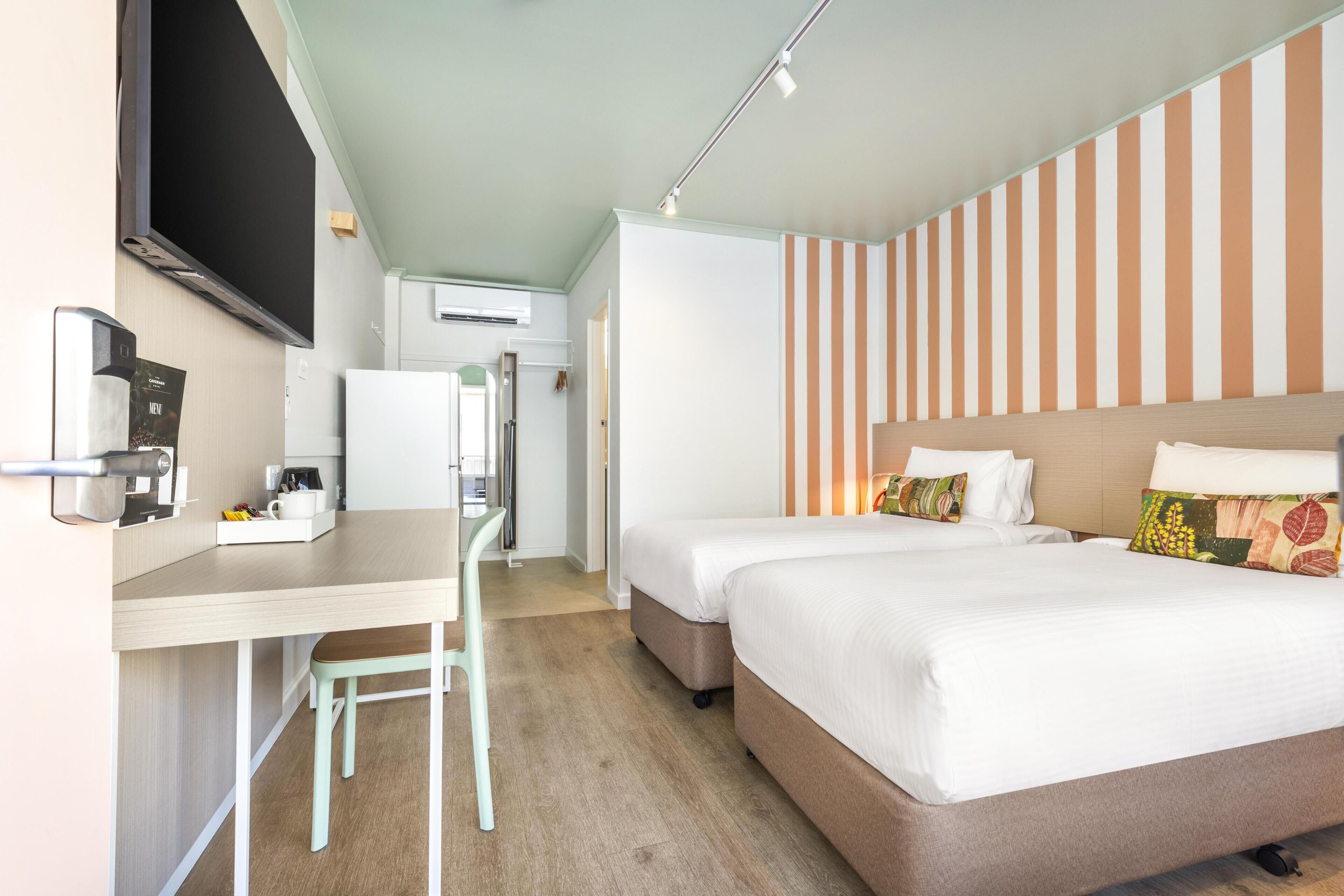 A hotel room with a bed, a desk, a chair, a television, and a striped wall.
