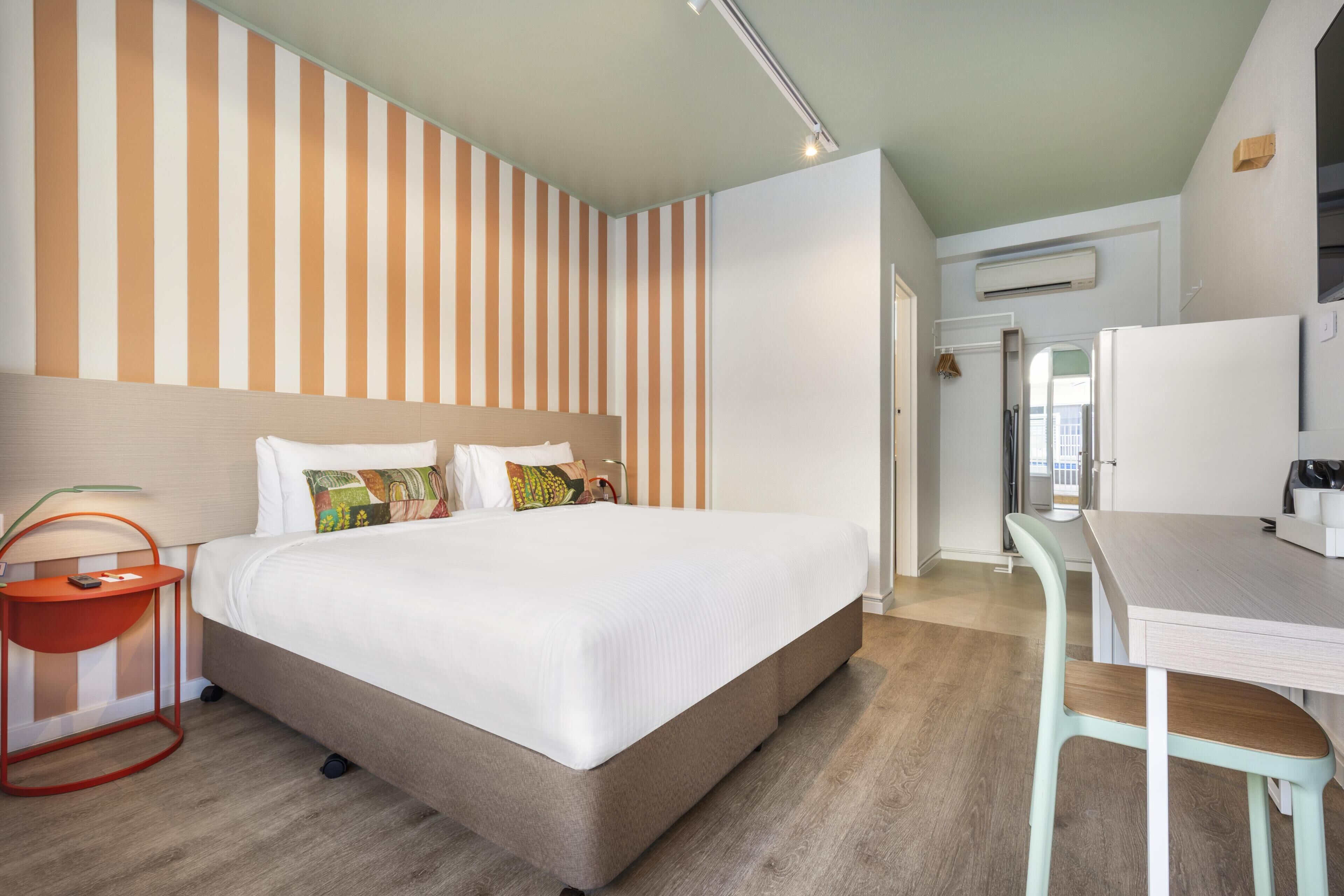 Habitació d'hotel amb un llit gran, una taula de treball i un mur a ratlles.