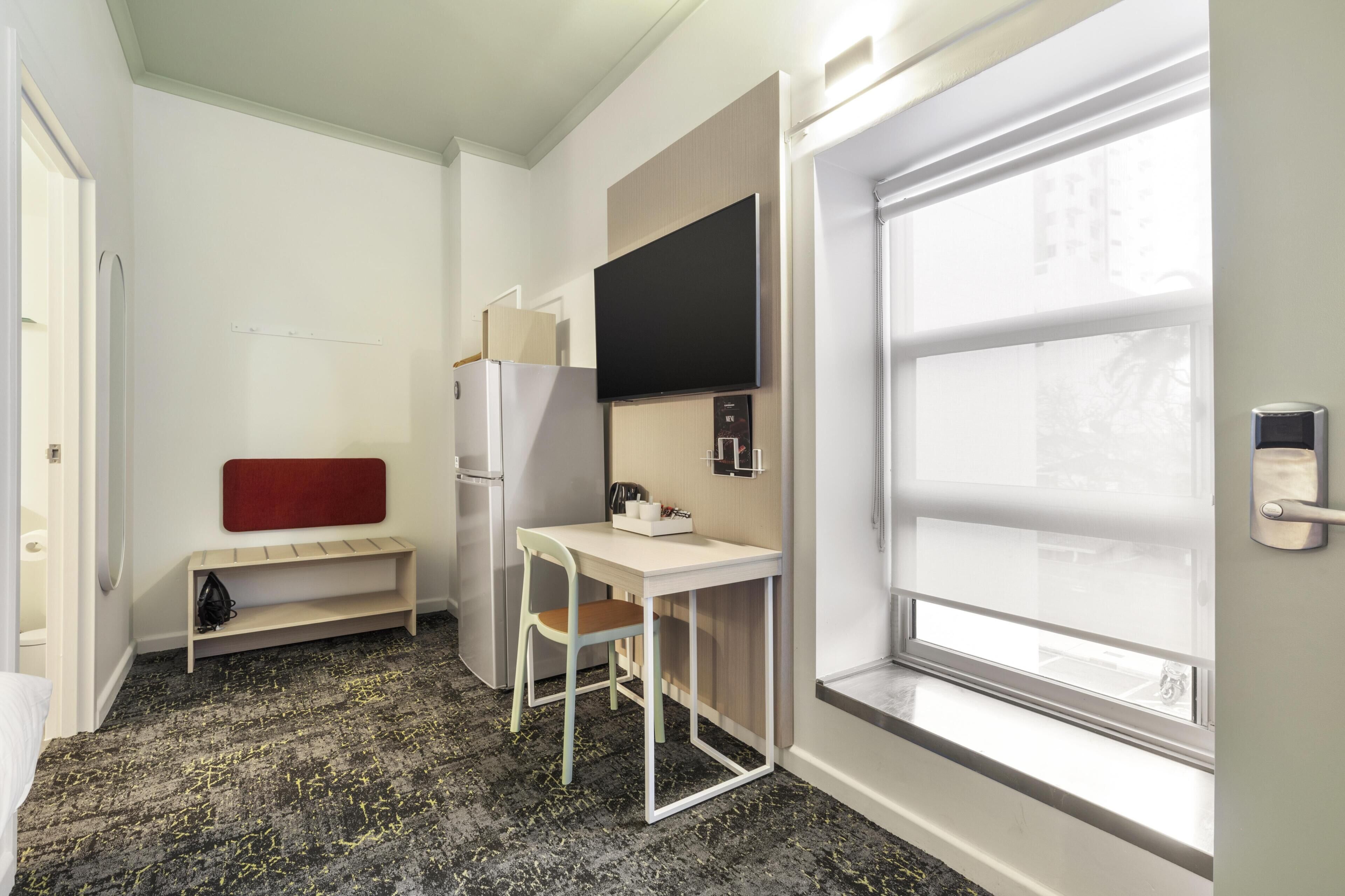 A hotel room with a desk, chair, and a flat-screen TV mounted on the wall.