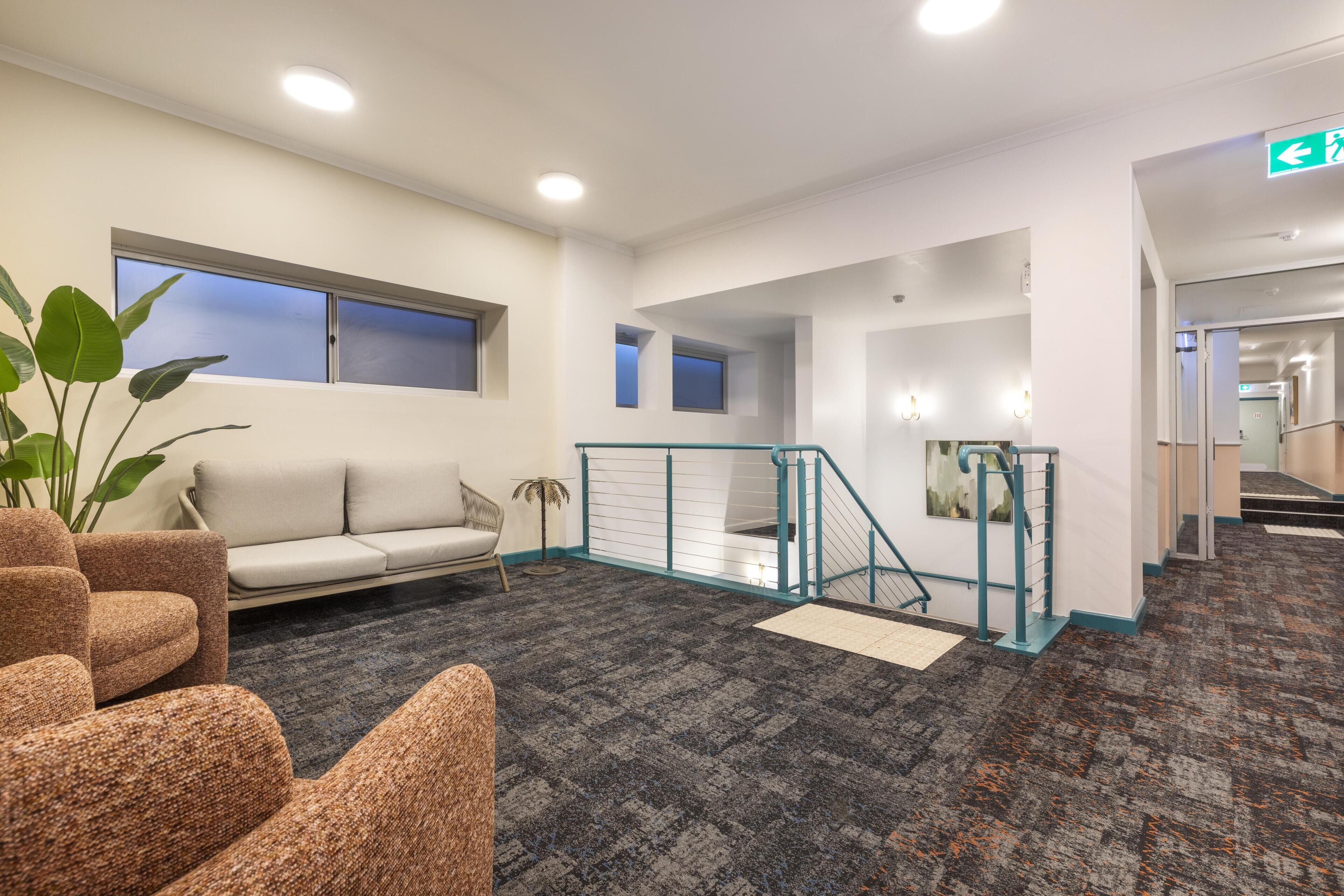 A hotel lobby with a sofa, chairs, a staircase, and a plant.