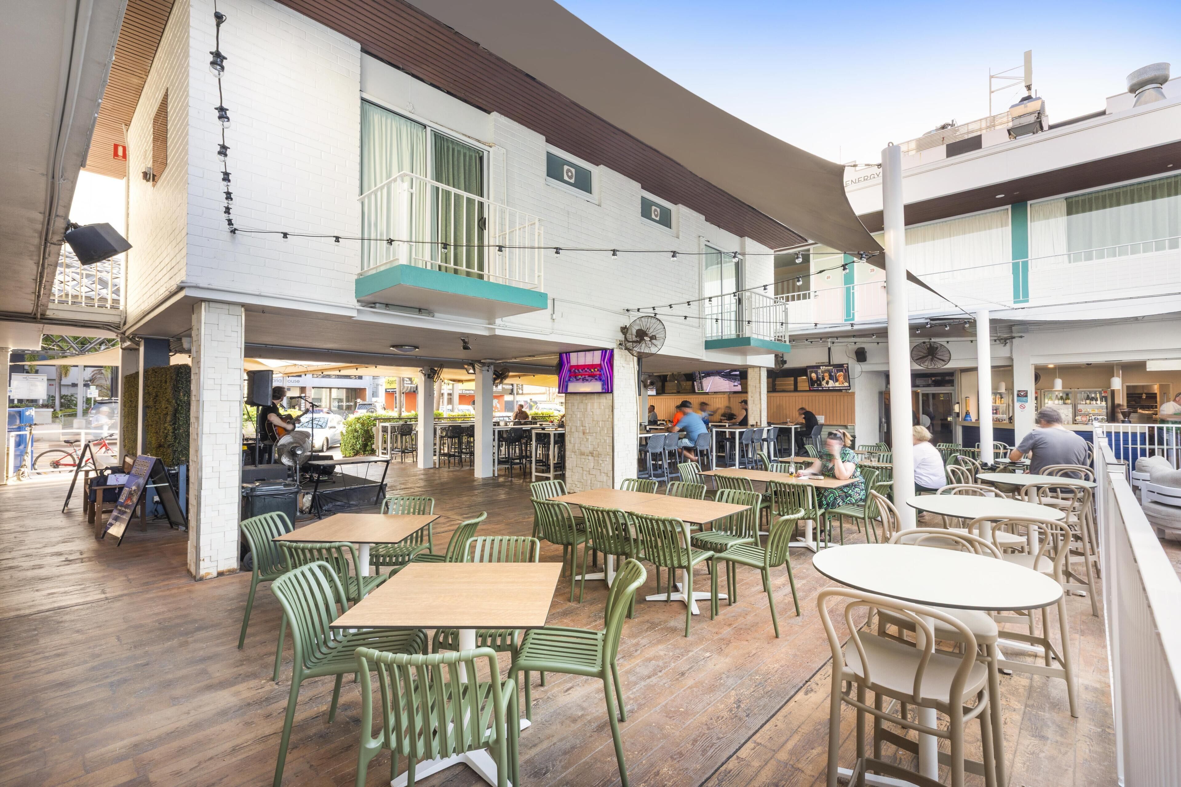 An outdoor cafe with tables and chairs, a building with a balcony, and a clock on the wall.