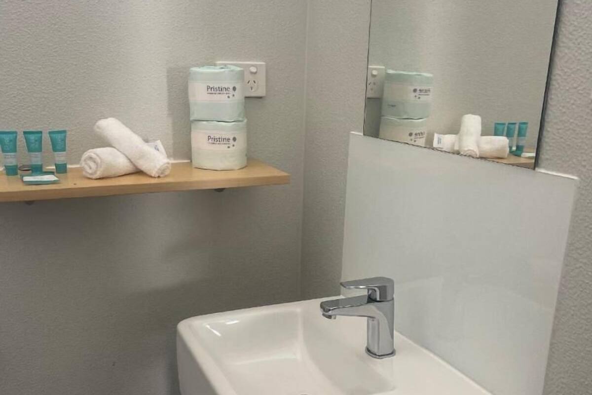 Un baño con un lavamanos blanco, un espejo y un estante con artículos de aseo.
