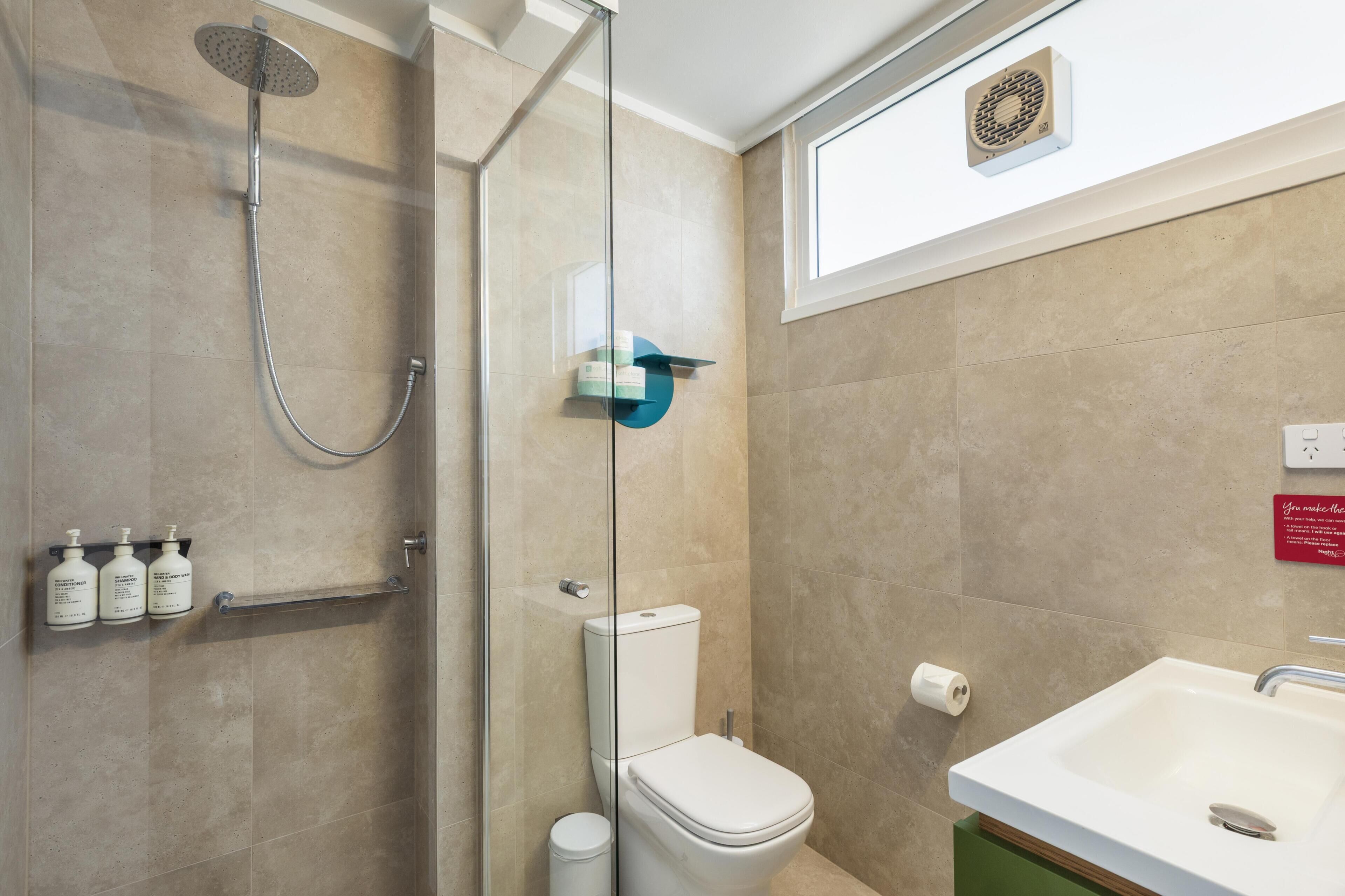 Un baño con ducha de vidrio, inodoro, lavamanos y dispensador de toallas.