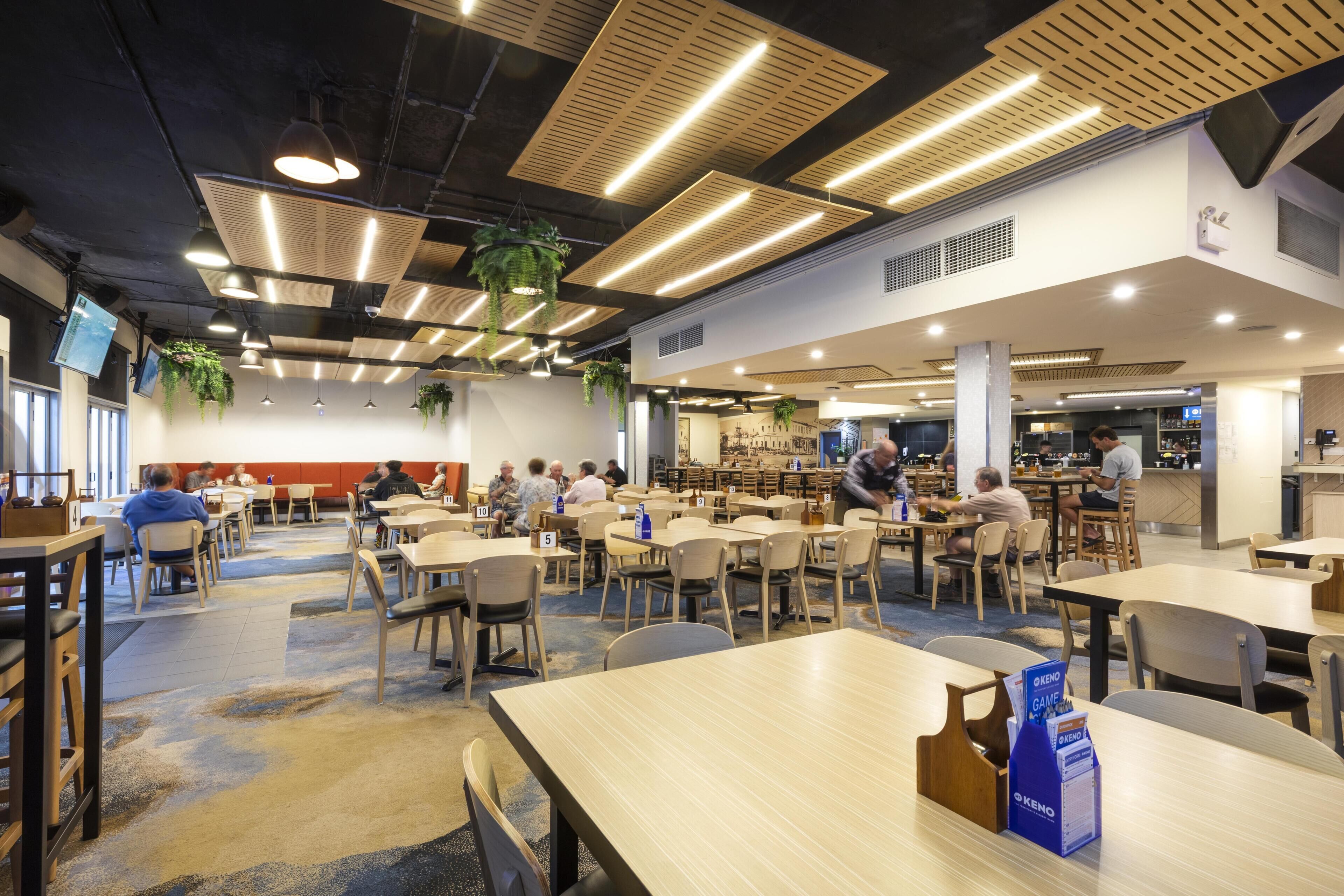 A spacious indoor dining area with multiple tables and chairs, ceiling lights, and hanging plants.