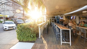 An outdoor café with tables and chairs, a covered seating area, and a view of the street with cars. - Nightcap at the Cavenagh (Darwin)
