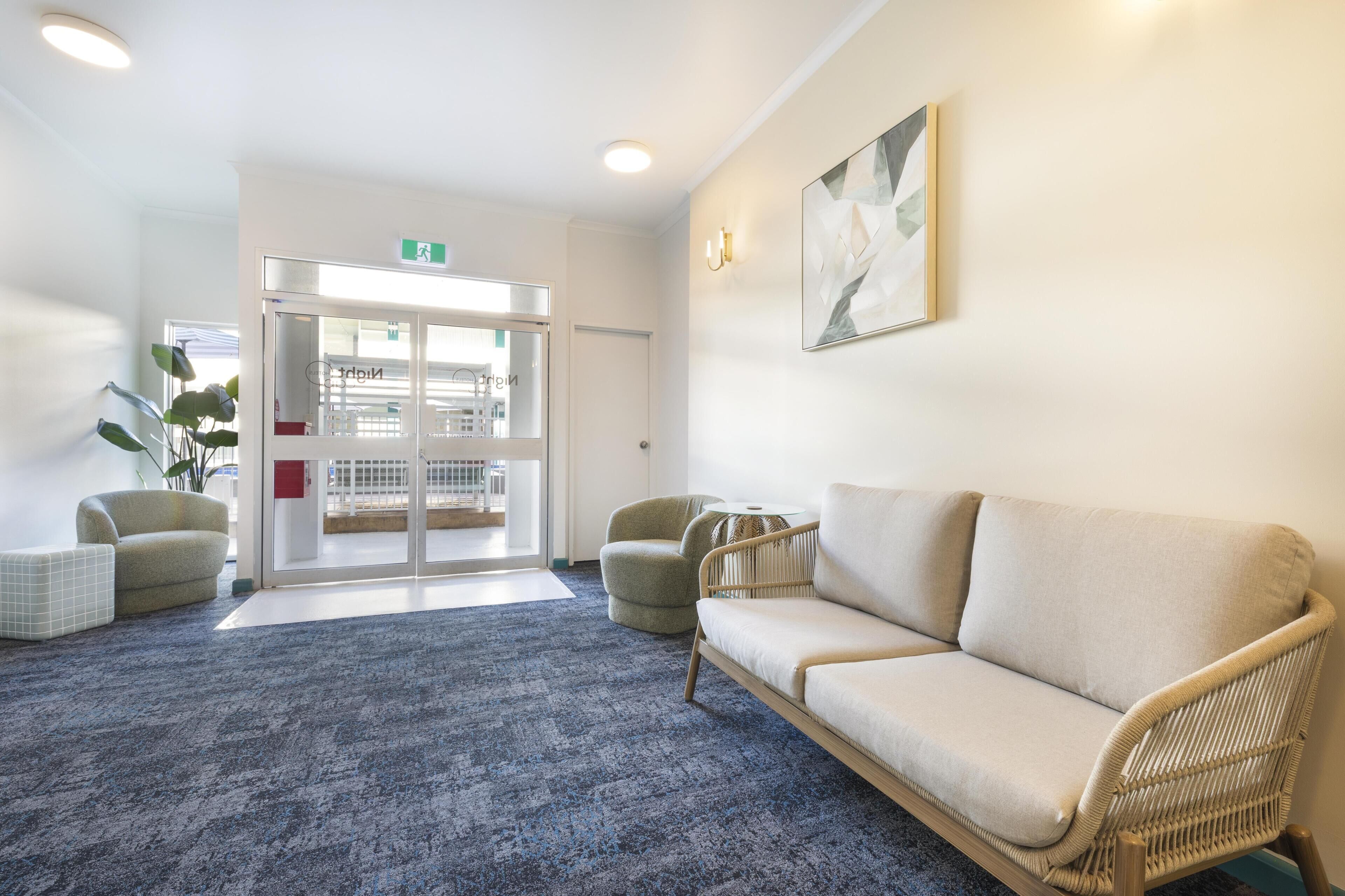 A reception area with a blue carpet, a sofa, two armchairs, a glass door entrance, and a wall-mounted light fixture.