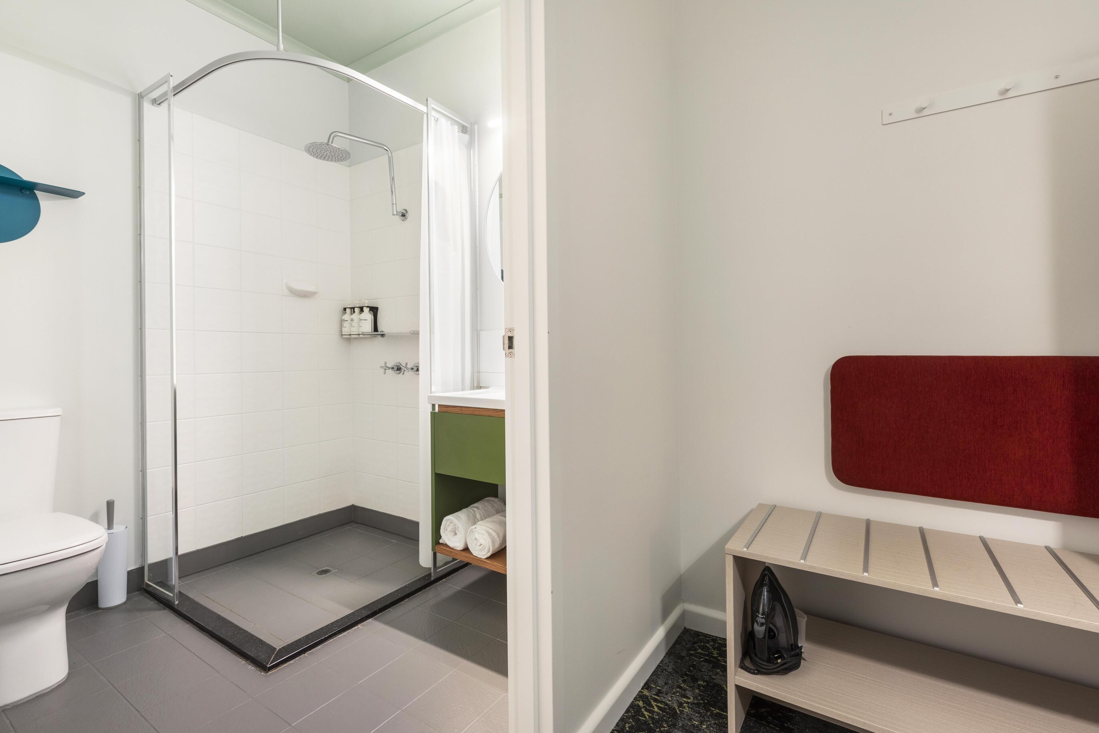 Een badkamer met toilet, douche en een plank met handdoeken.