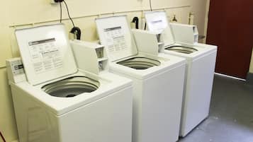 A row of white front-loading washing machines with instruction manuals open, connected to a power outlet on the wall.