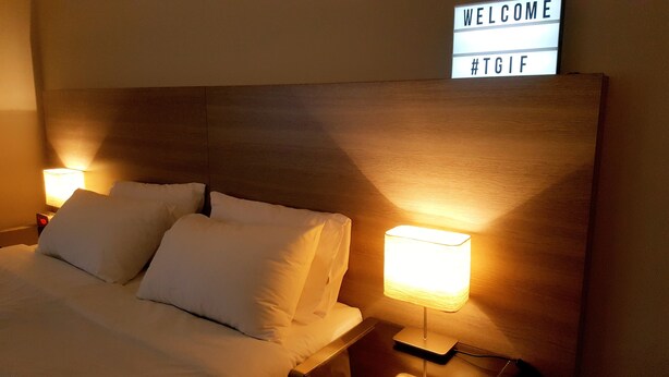 A hotel room with a neatly made bed, two bedside lamps, and a 'WELCOME' sign with a hashtag. - City Waters Perth (Perth)