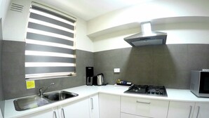 A modern kitchen with white cabinets, a stainless steel sink, a gas stove, a microwave, and a window with blinds. - City Waters Perth (Perth)