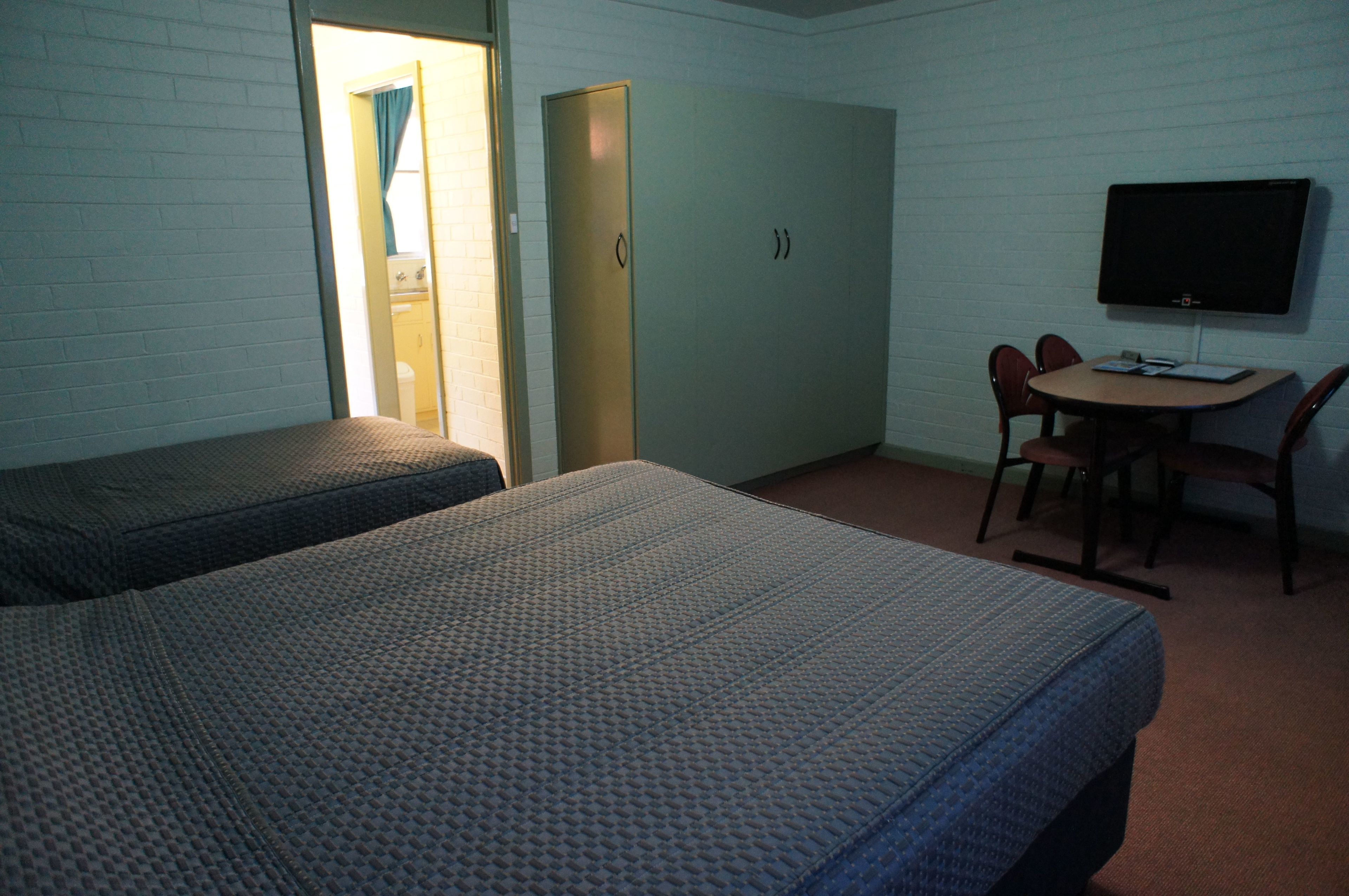 A room with two beds, a desk with a chair, a television, and a door leading to a bathroom.