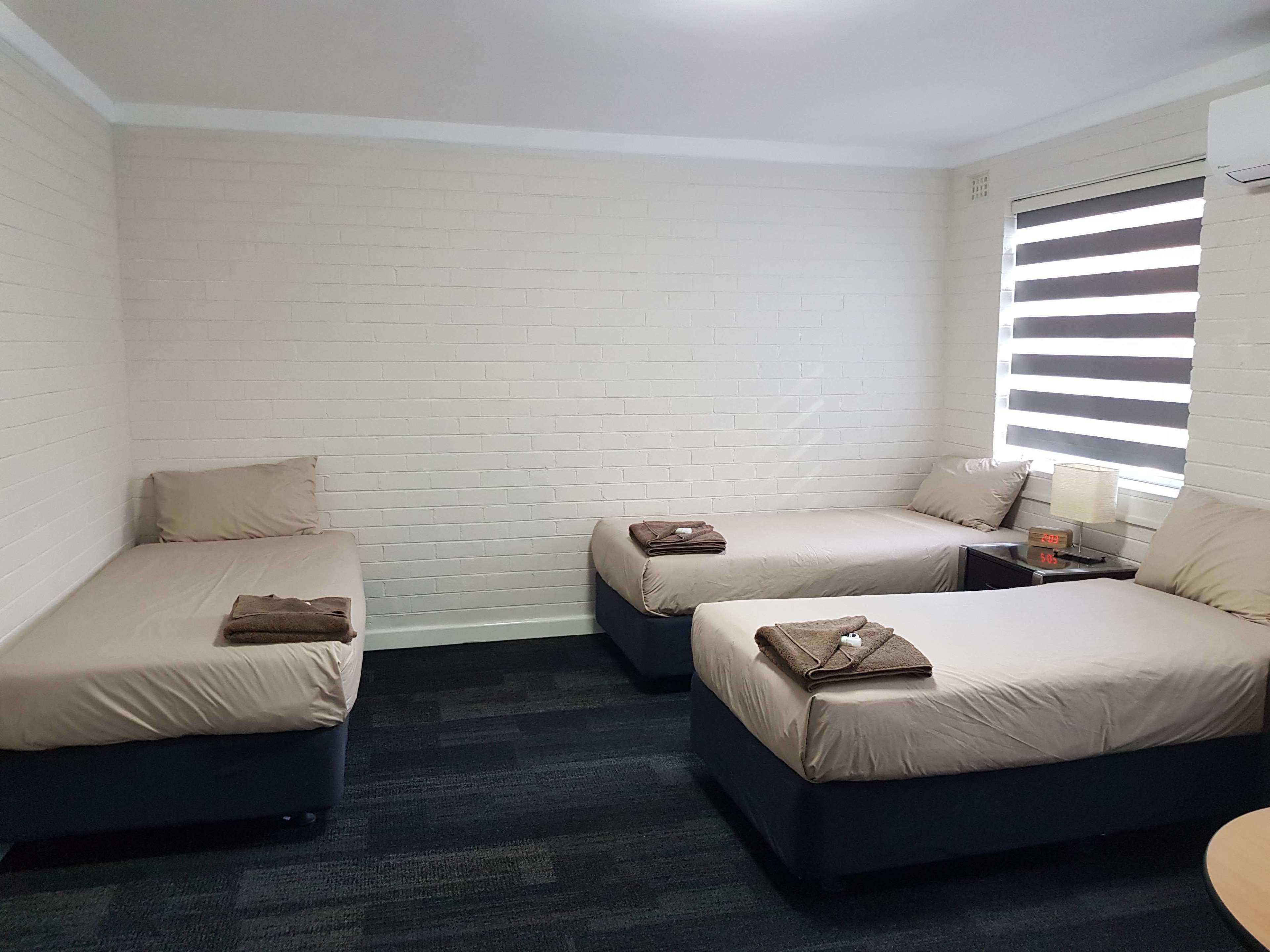 Een kamer met twee eenpersoonsbedden, een tafeltje en een raam met zonwering.
