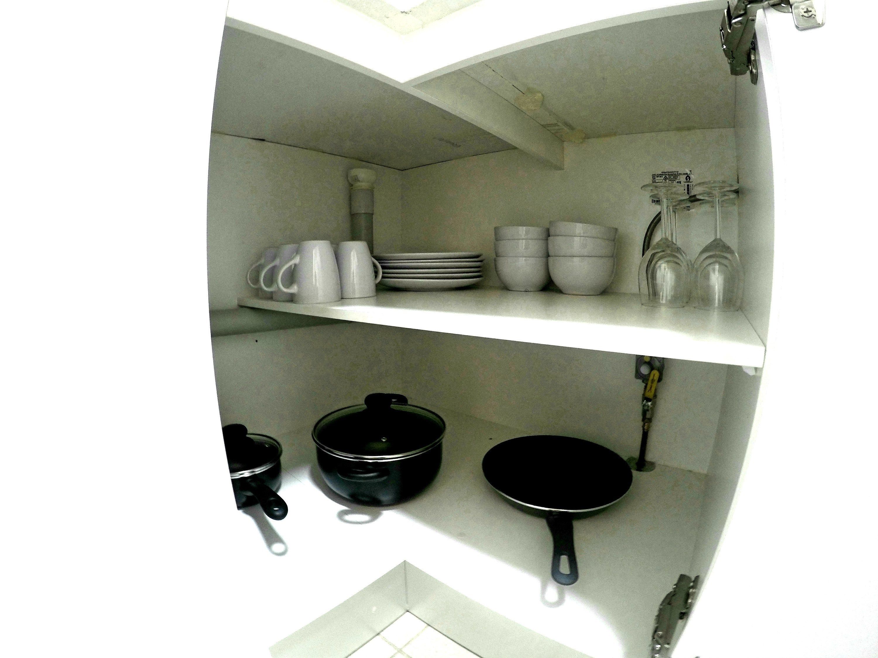 A kitchen with white shelves holding mugs, bowls, and a frying pan.