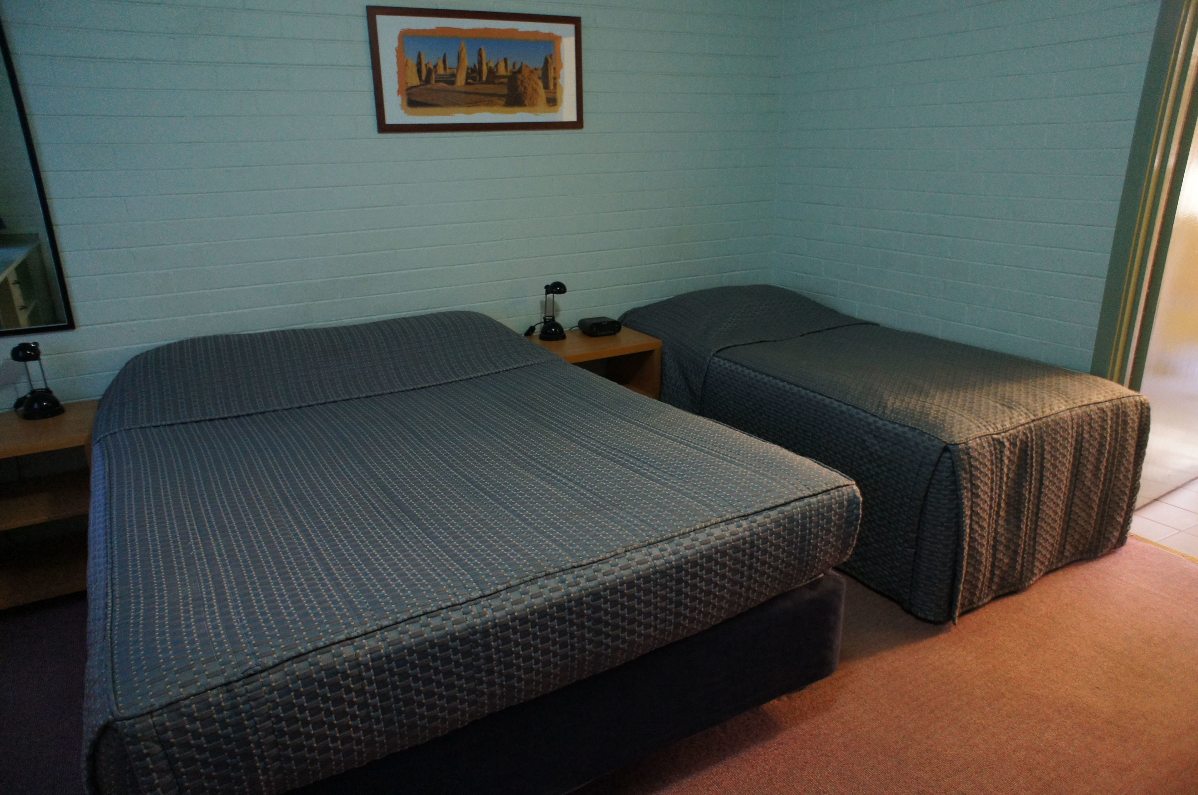 Una habitación con dos camas, una mesita de noche, una lámpara y un cuadro en la pared.