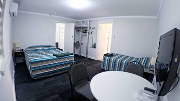A compact hotel room with two beds, a small table, a chair, a TV, and a closet with hanging clothes.