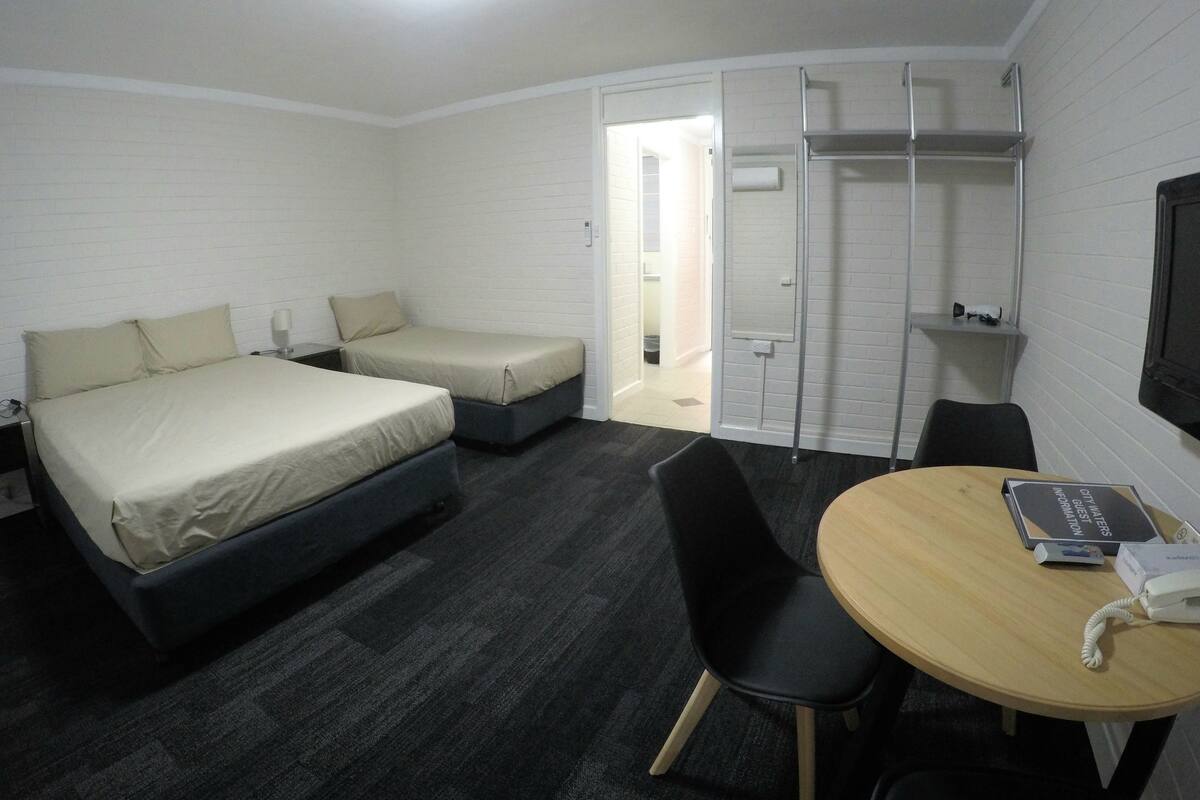 Quarto de hotel com duas camas, uma escrivaninha com cadeira, televisão e porta para o banheiro.