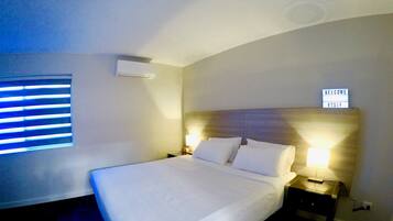 A hotel room with a large bed, two bedside lamps, a wall-mounted air conditioner, and a window with blinds.