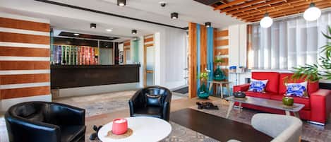 Un moderno vestíbulo de hotel con una recepción, asientos de cuero, un sofá rojo y una alfombra estampada.