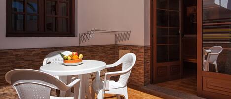 A patio with a round table and white chairs, a fruit bowl, and a metal drying rack.