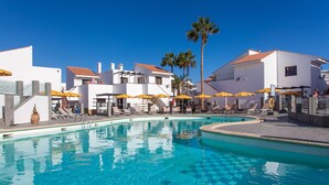 A swimming pool with lounge chairs and umbrellas, surrounded by white buildings with red-tiled roofs. - Apartamentos Villa Florida (Antigua)